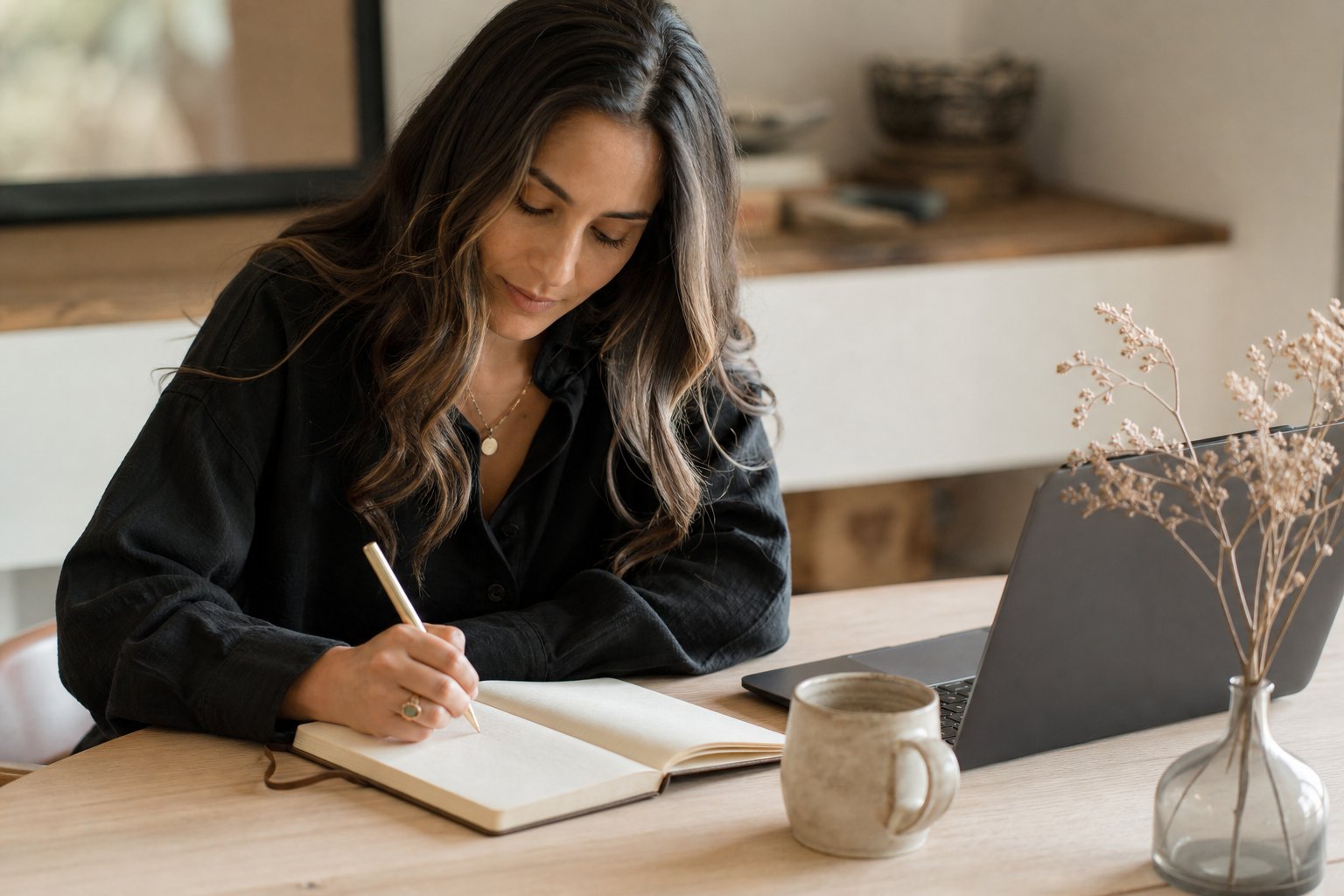 Wedding planner writing a weekly plan in a notebook beside a laptop