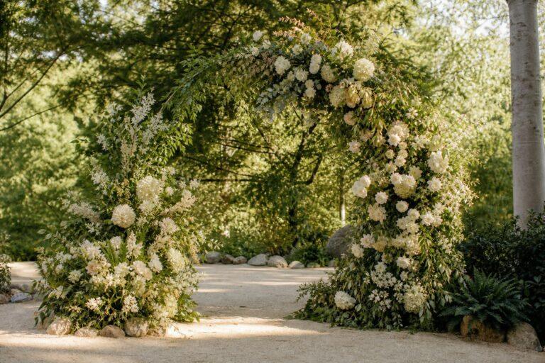wedding flower installation on a ceremony arch with greenery and cream blooms